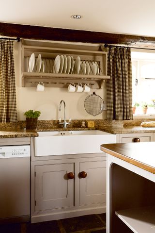 A country kitchen with neutral cabinetry, wood knobs, traditional crockery dish rack shelving and a butler's sink