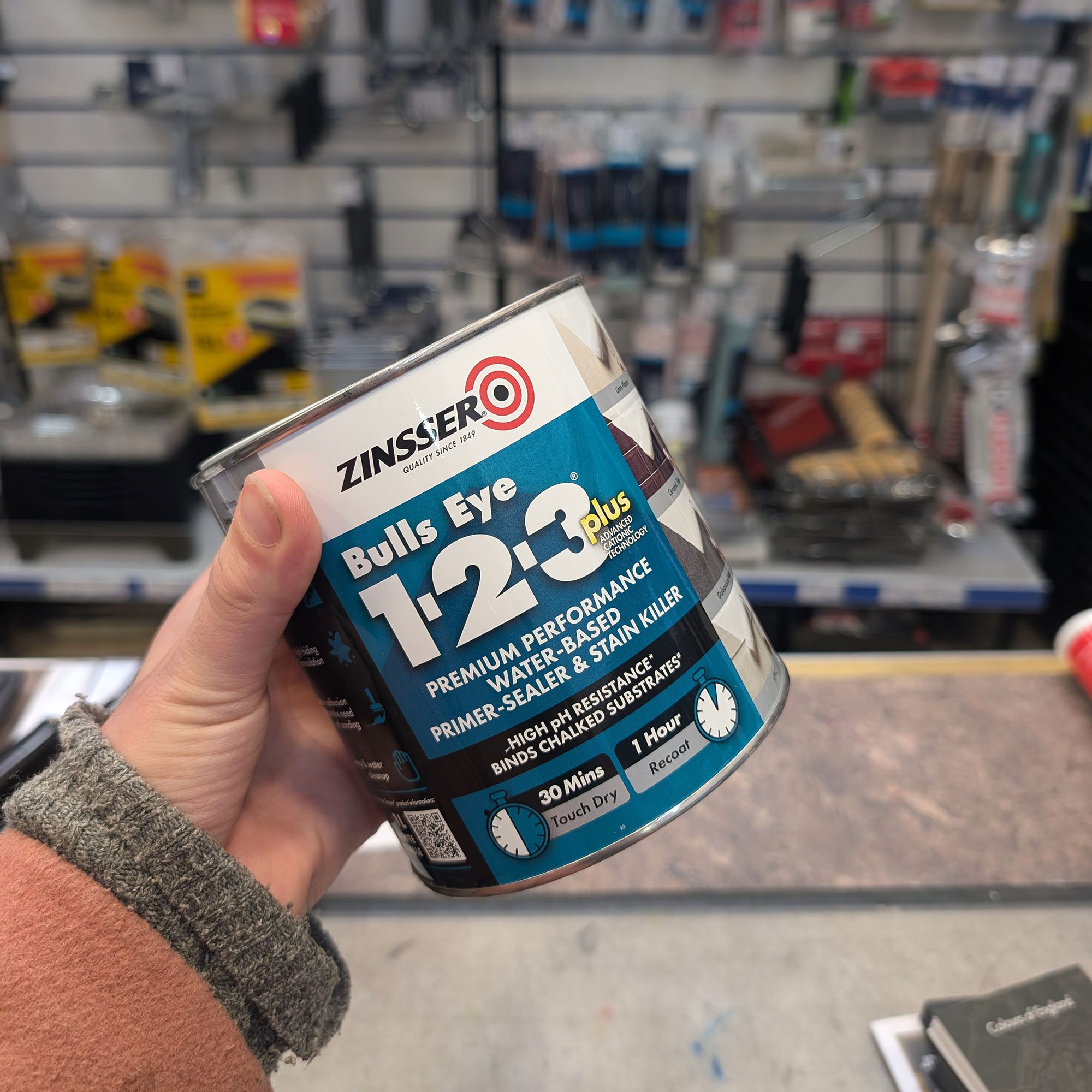 Hand holding tin of paint in hardware shop