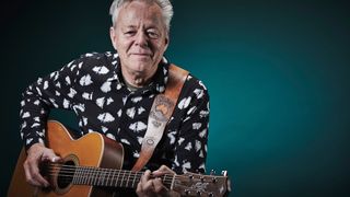 Tommy Emmanuel playing guitar in front of a turquoise background