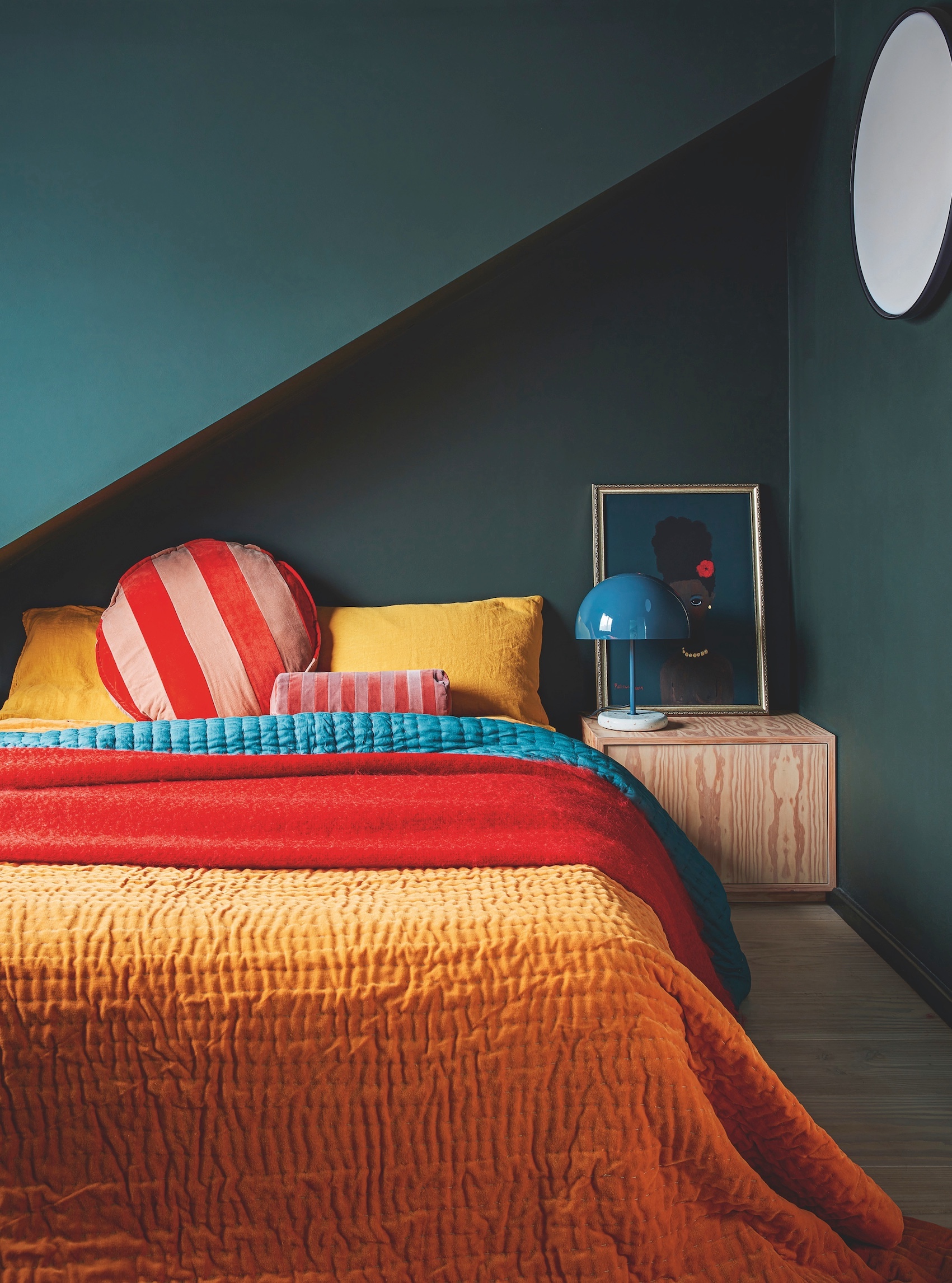 teal bedroom with orange bed cover, yellow pillows and bright cushions and throws