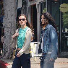 Lily Rose Depp wearing a teal shirt, beige hoodie, indigo jeans, suede shoulder bag, and tan suede loafers