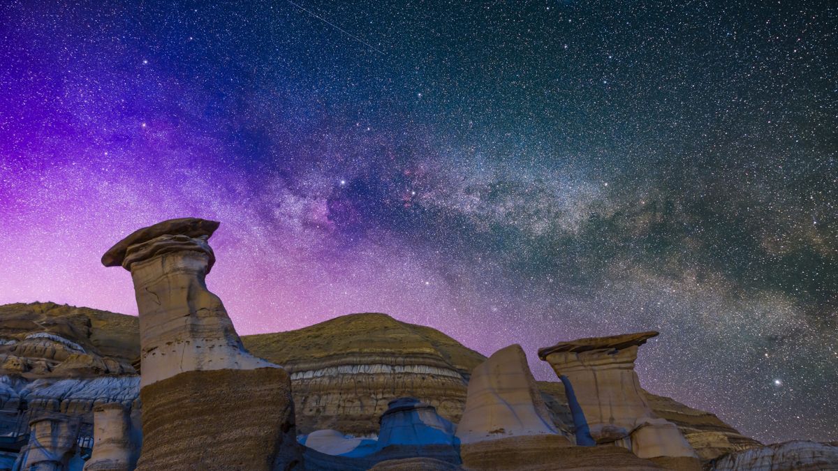 The summer Milky Way in Cygnus, with the Summer Triangle stars rising over the Hoodoos formations on Highway 10 near Drumheller, Alberta. A low-level aurora display tints the sky magenta and blue at left, making for an unusually colourful sky. The bright stars are: Vega is at top, Deneb at centre and Altair at bottom right.