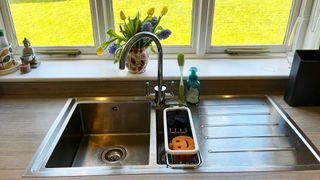 Stainless steel sink with a curved spout tap and a sink caddy with sponges in it.