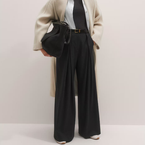 A model wearing black wide-;eg trousers, a bag and coat