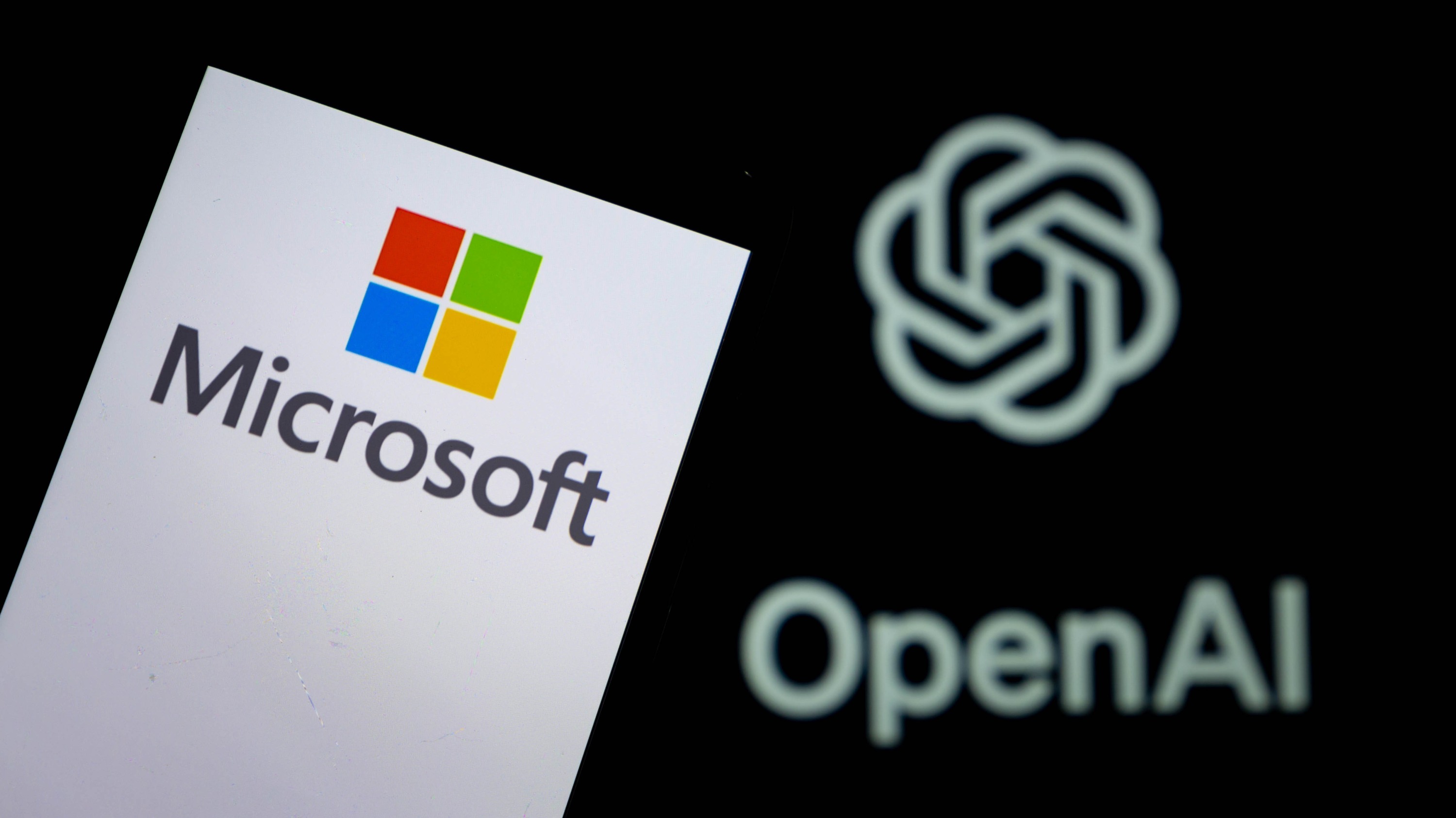The Microsoft logo displayed on a smartphone with the OpenAI logo in the background.