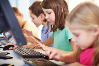 Elementary school kids work at desktop computers.