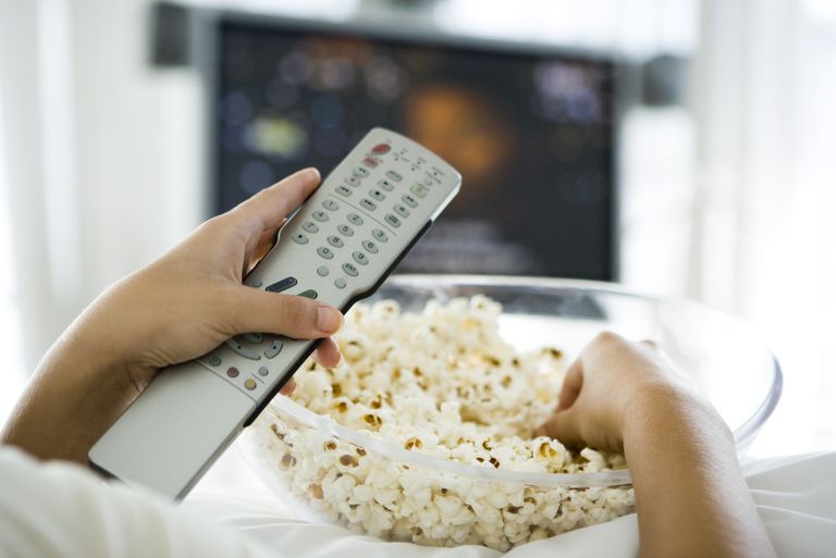 TV series - best Netflix comedies: Shutterstock image of popcorn in glass bowl infront of TV with remote in hand