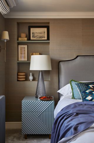 bedroom with brown wallpaper, grey upholstered bed, alcove/beddroom storage, large bedside lamp