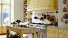 yellow vintage style kitchen with hanging copper pots and a large farmhouse style cooker hood