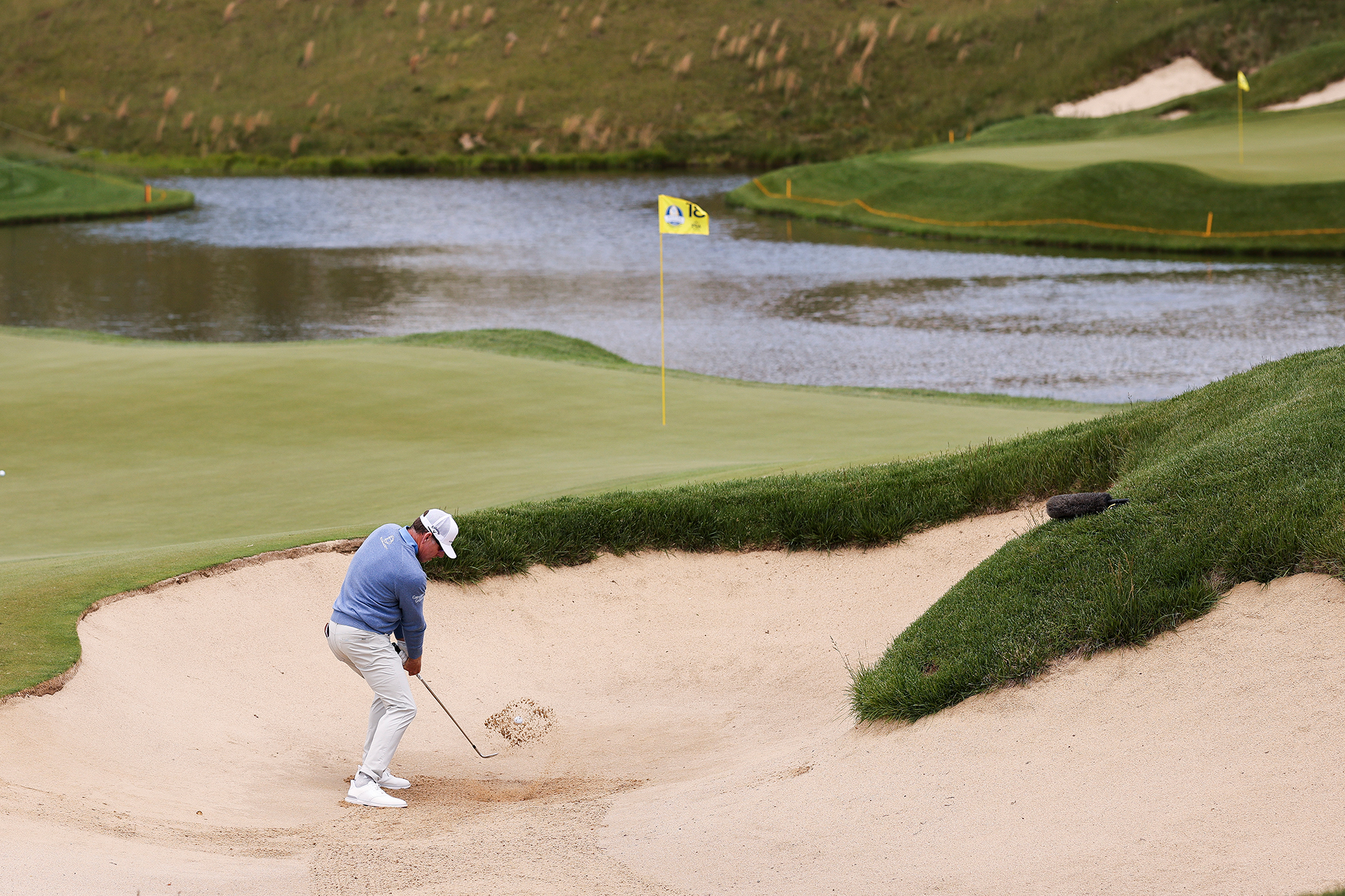Justin Leonard hitting a bunker shot towards a pin with water behind the green