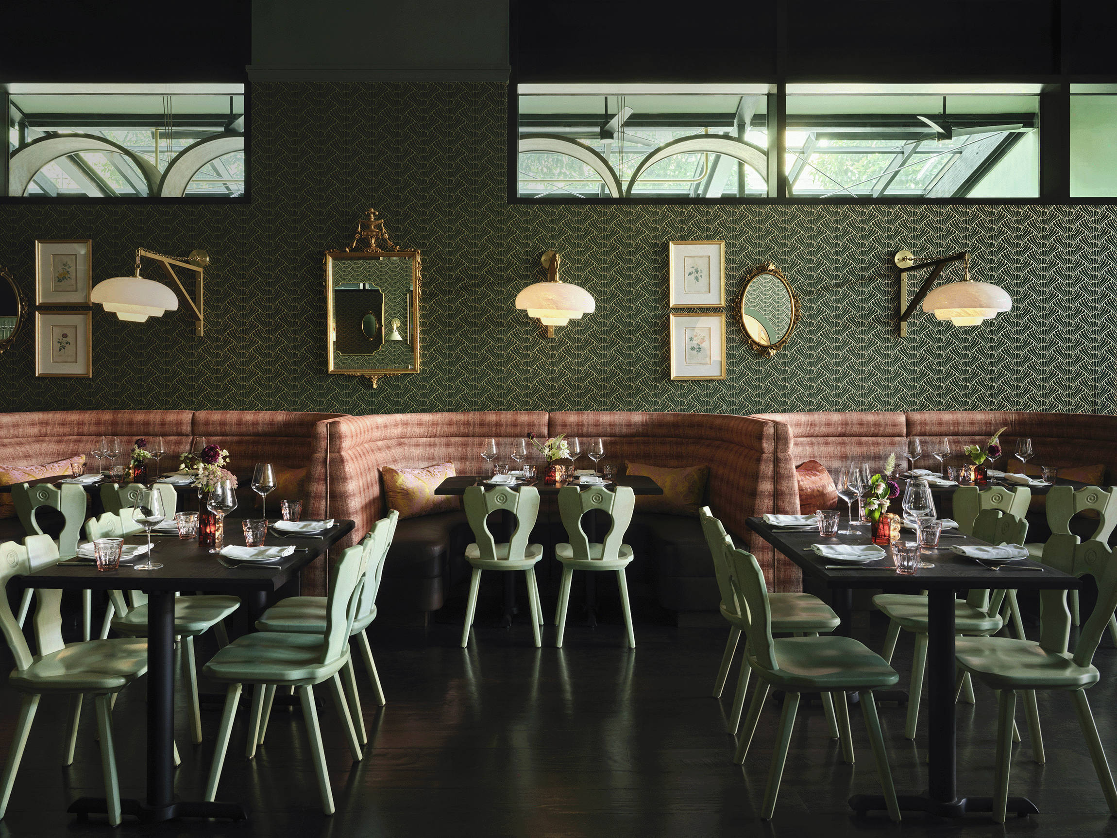 A bistro-style restaurant with mint green, heart-shaped chairs, pink banquettes, textural mint wallpaper, and gold-framed artworks and mirrors.