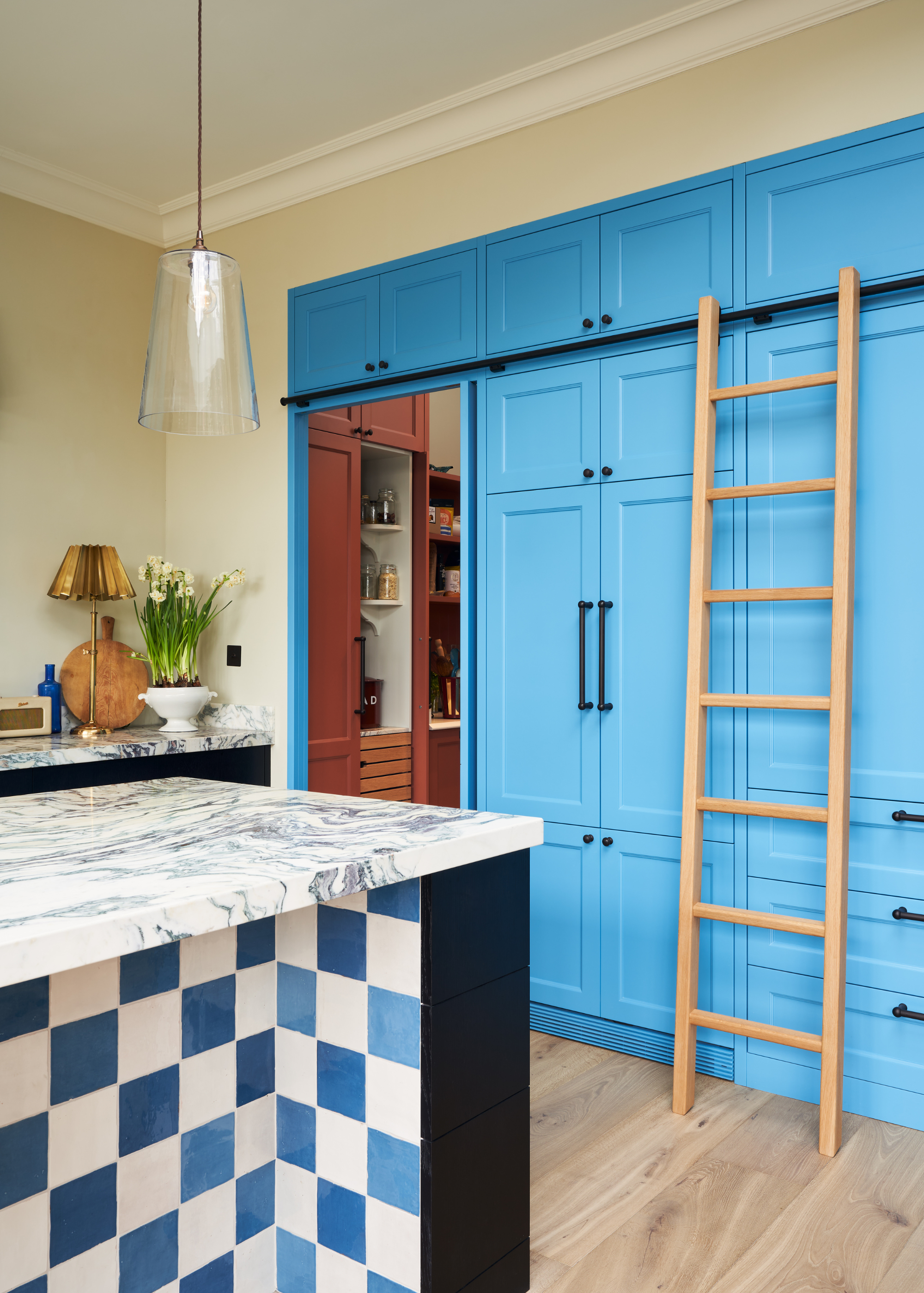 blue kitchen cabinetry w a ladder leading into a pantry with red cabinets
