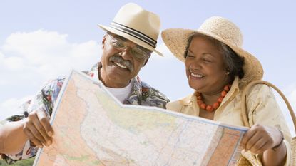 A retired couple smile as they look at a map while out and about.