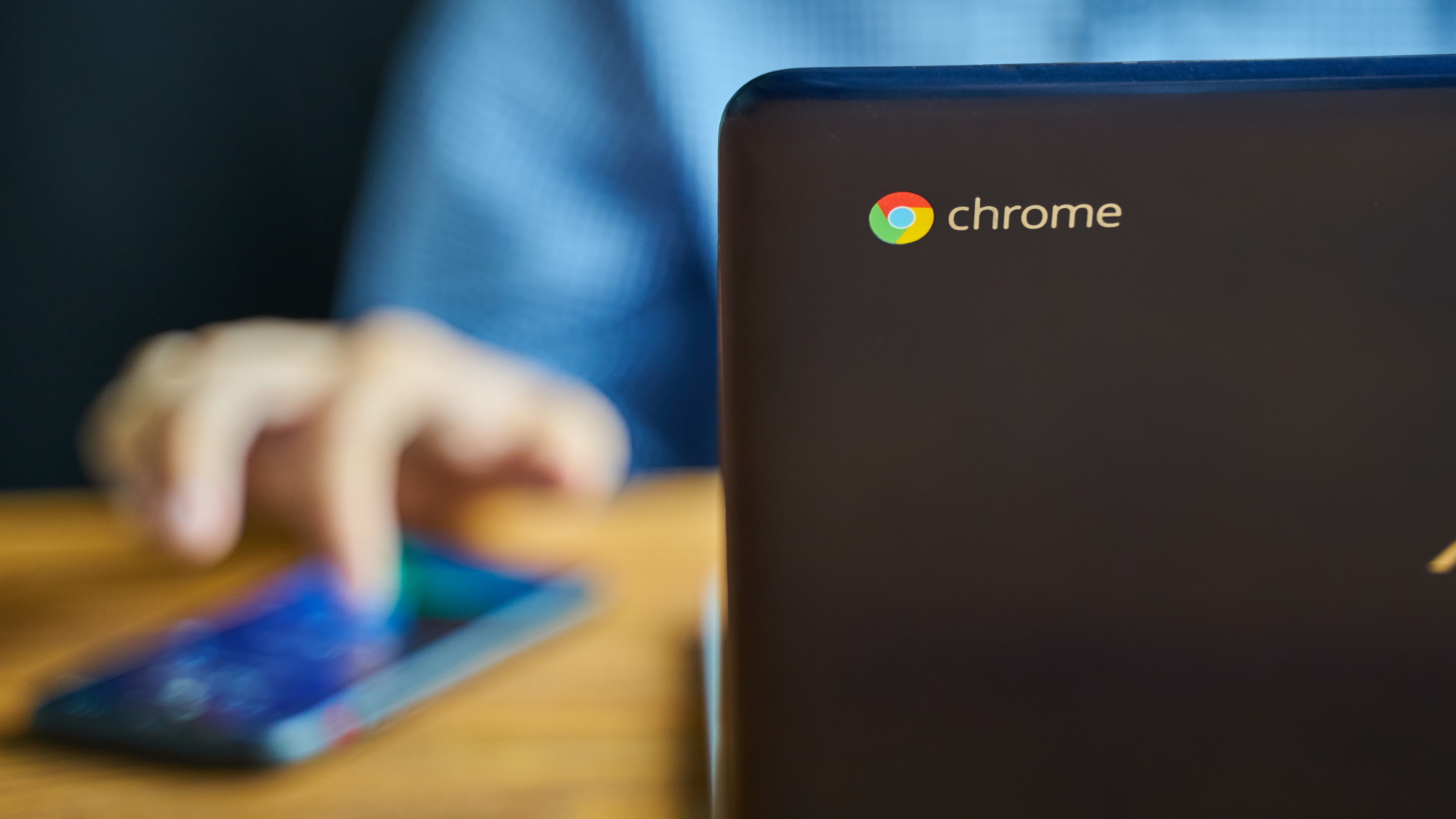 Chrome logo on the back of a Chromebook with a man out of focus working on it