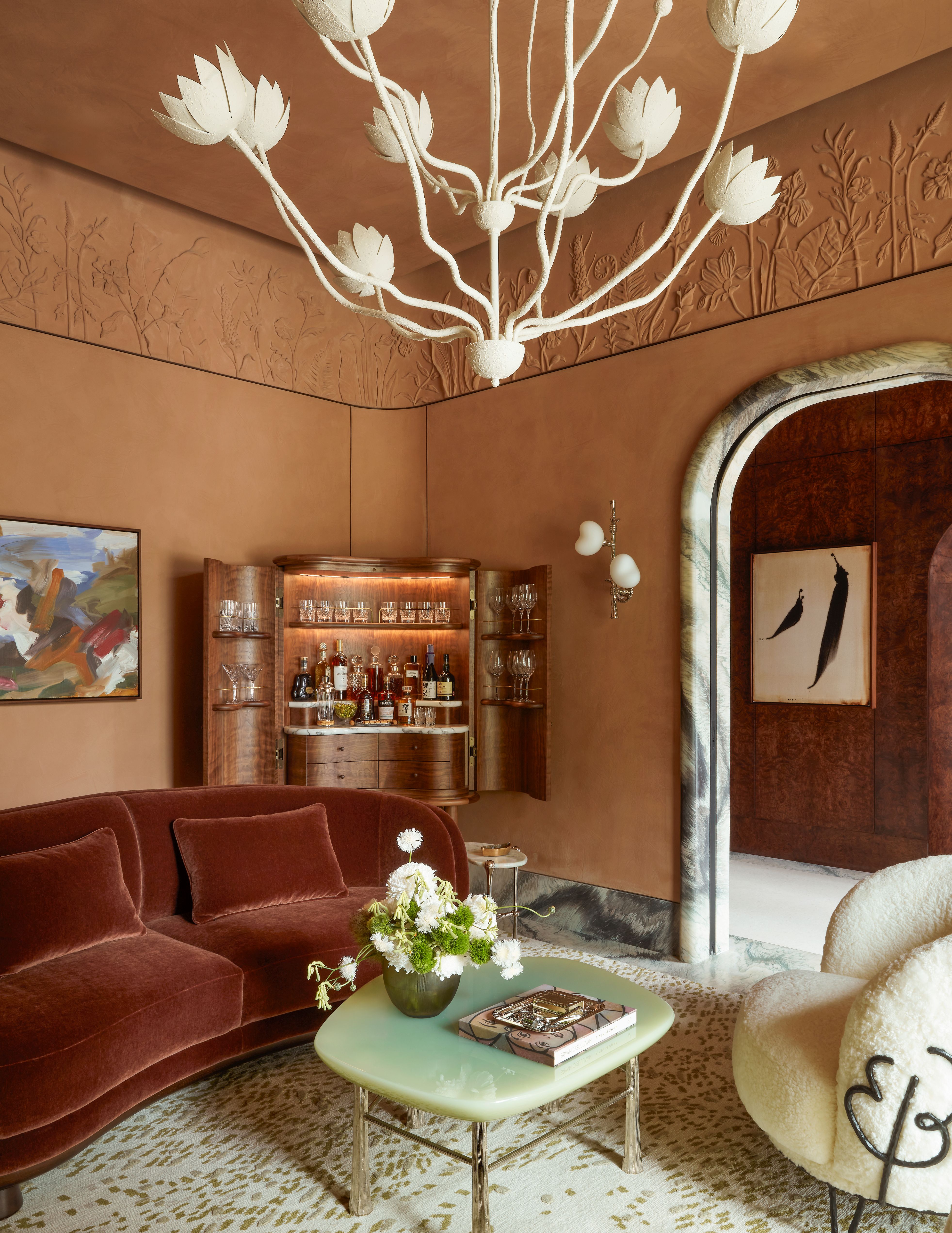 beautiful art deco sitting room with terracotta walls, a white chandelier, and curved furniture