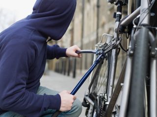 A person in a hoodie breaking a bike lock with bolt cutters