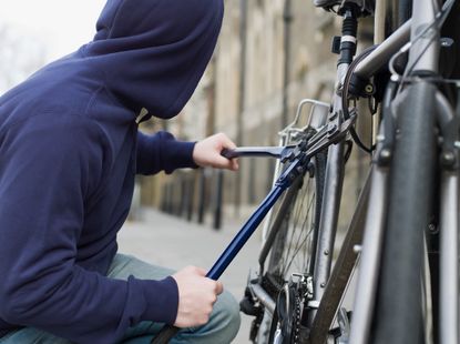 A person in a hoodie breaking a bike lock with bolt cutters