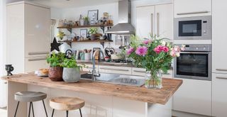 cream kitchen with kitchen island with wooden countertop and stools with houseplants t suggest how to make a kitchen smell good