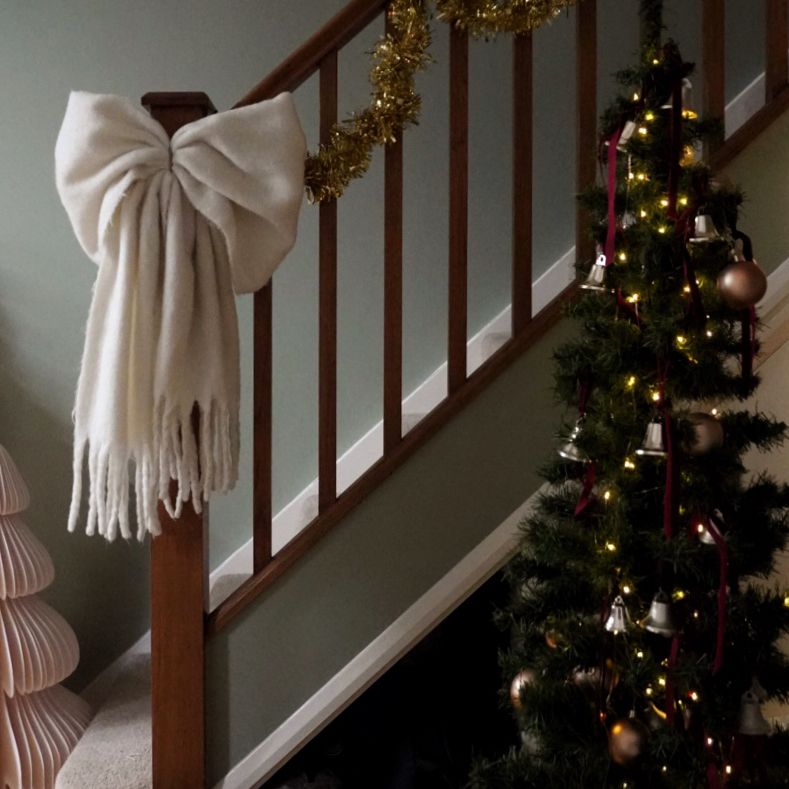 bannister with christmas tree and large white bow tied to the end