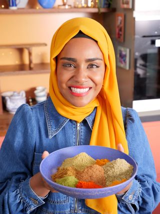Nadiya Hussain holding a bowl filled with colourful spices.