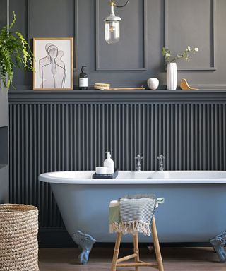 A blue clawfoot bath sitting in a bathroom with grey panelled walls.