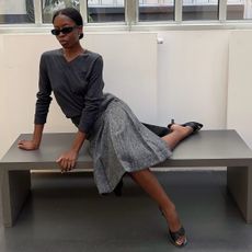 Sylvie Mus wearing a high v-neck, pleated skirt, and kitten-heel sandals.