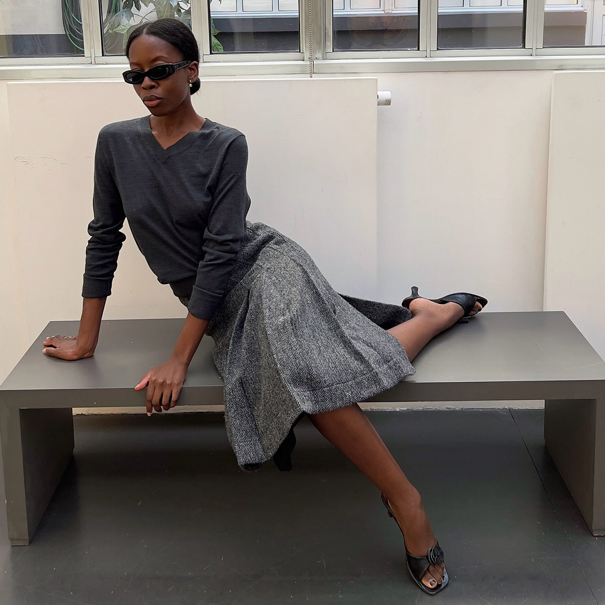 Sylvie Mus wearing a high v-neck, pleated skirt, and kitten-heel sandals.