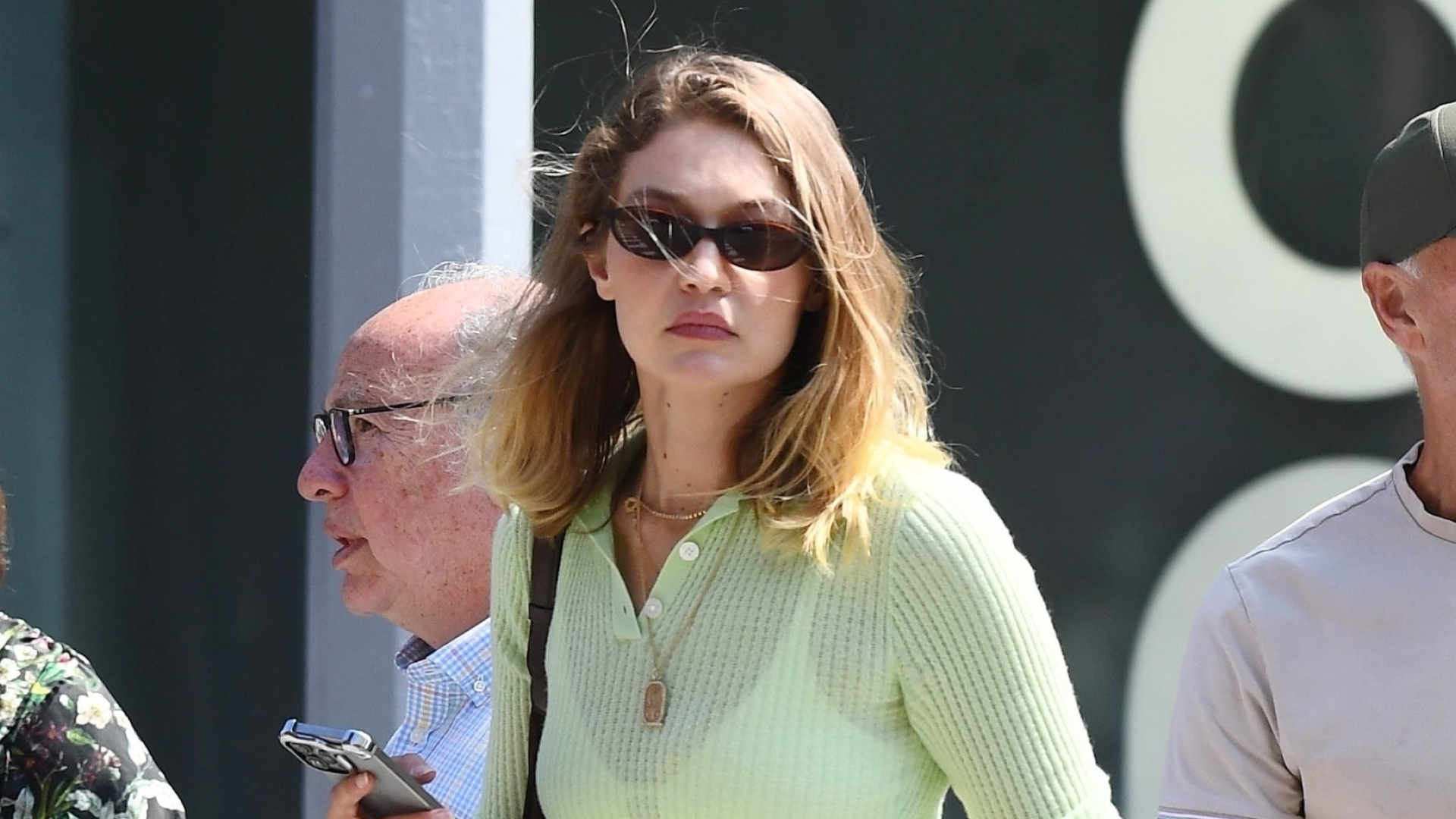 Gigi Hadid wearing brown loafers, white linen pants, and a sheer green top