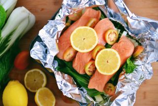 Salmon with slices of lemon and greens sitting in foill