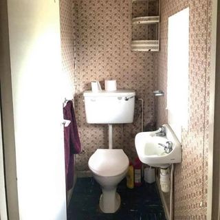 small toilet with wall hung sink and dated wallpaper
