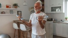 senior man does bicep curls with bottles of water in his kitchen