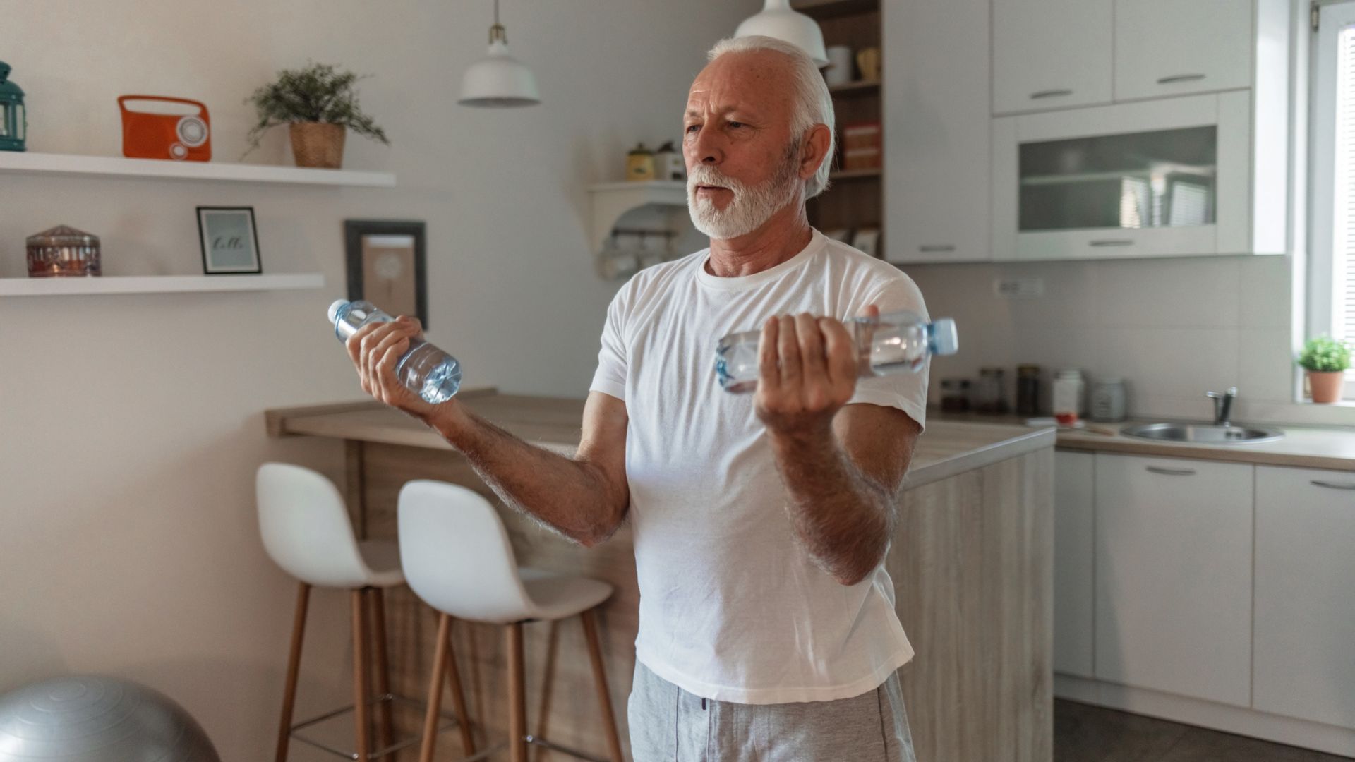 senior man does biceps curls with bottles of water in his kitchen