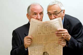 Two older men read a newspaper with surprise.