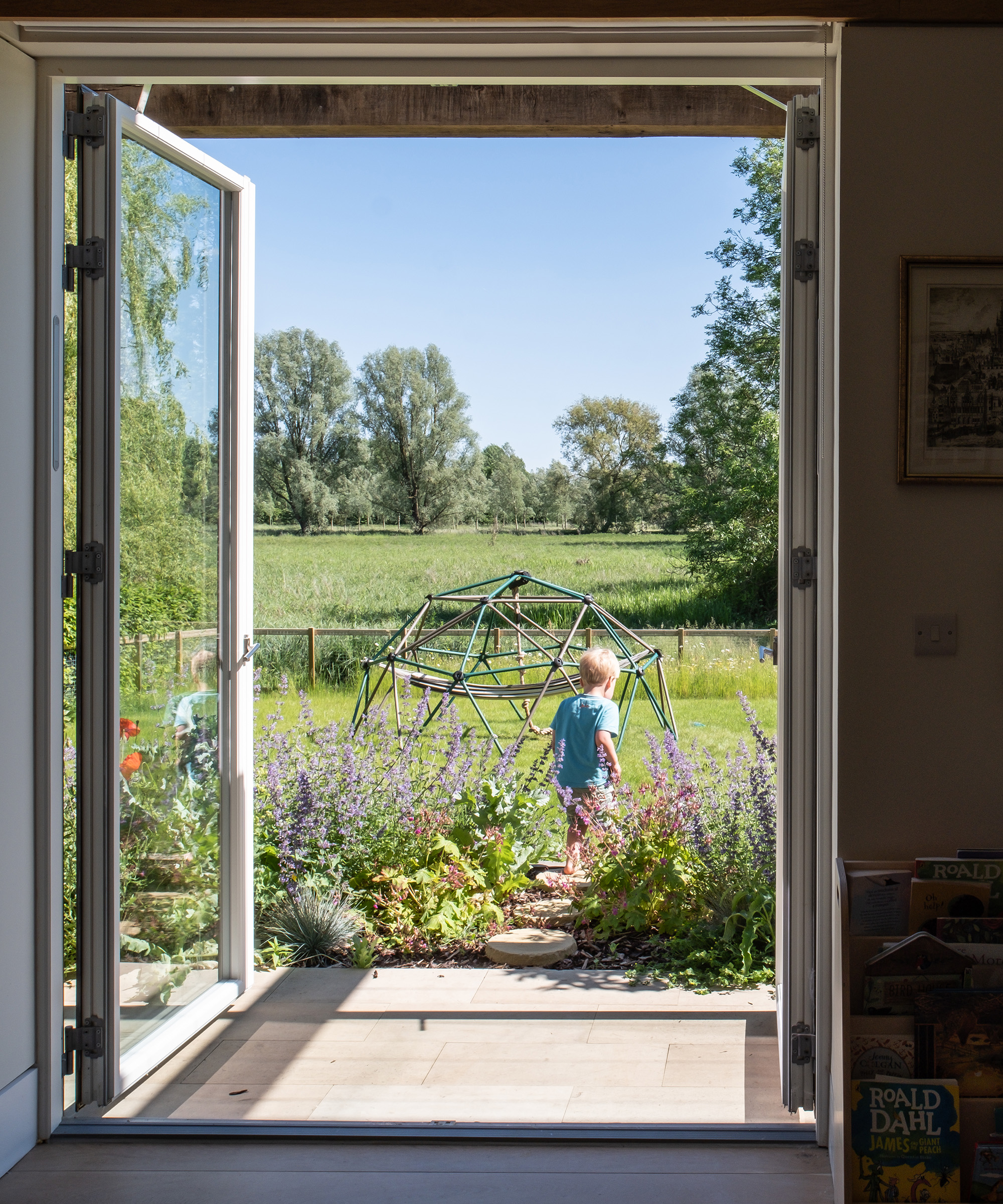 A child playing outside in a sunny garden with large glass doors looking out of a living room