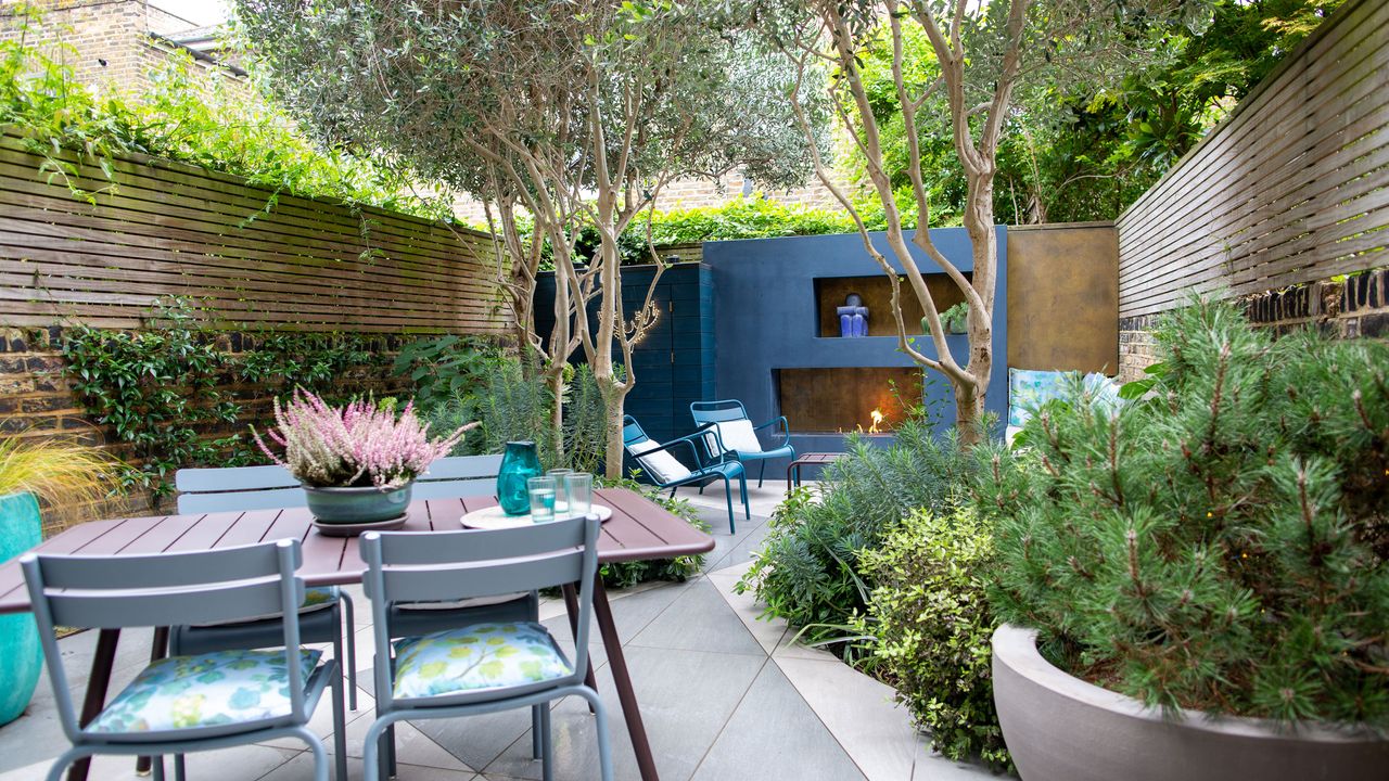 lush mediterranean oasis garden with blue painted wall and fireplace table and chairs