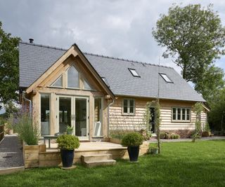 A small oak frame home with a pitched roof entrance with a tiny wooden patio at the front door