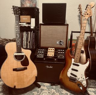 An acoustic guitar (left) and Stratocaster electric guitar (right) flank a trio of UAFX amp emulation pedals and a trio of combo amplifiers in the home of contributing writer Jimmy Leslie