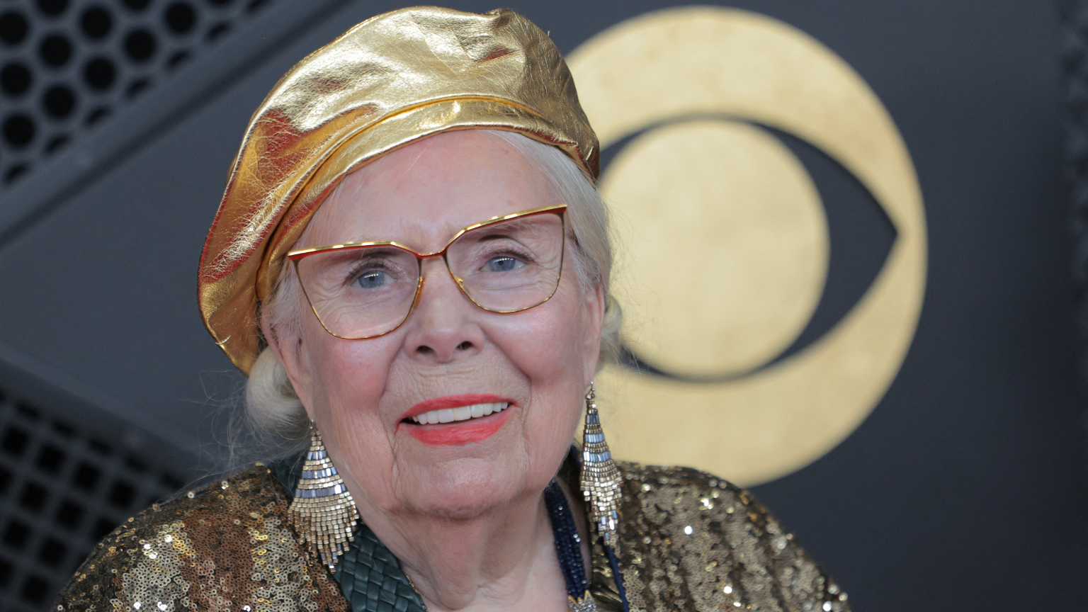 an older white woman with a red lipstick and gold outfit