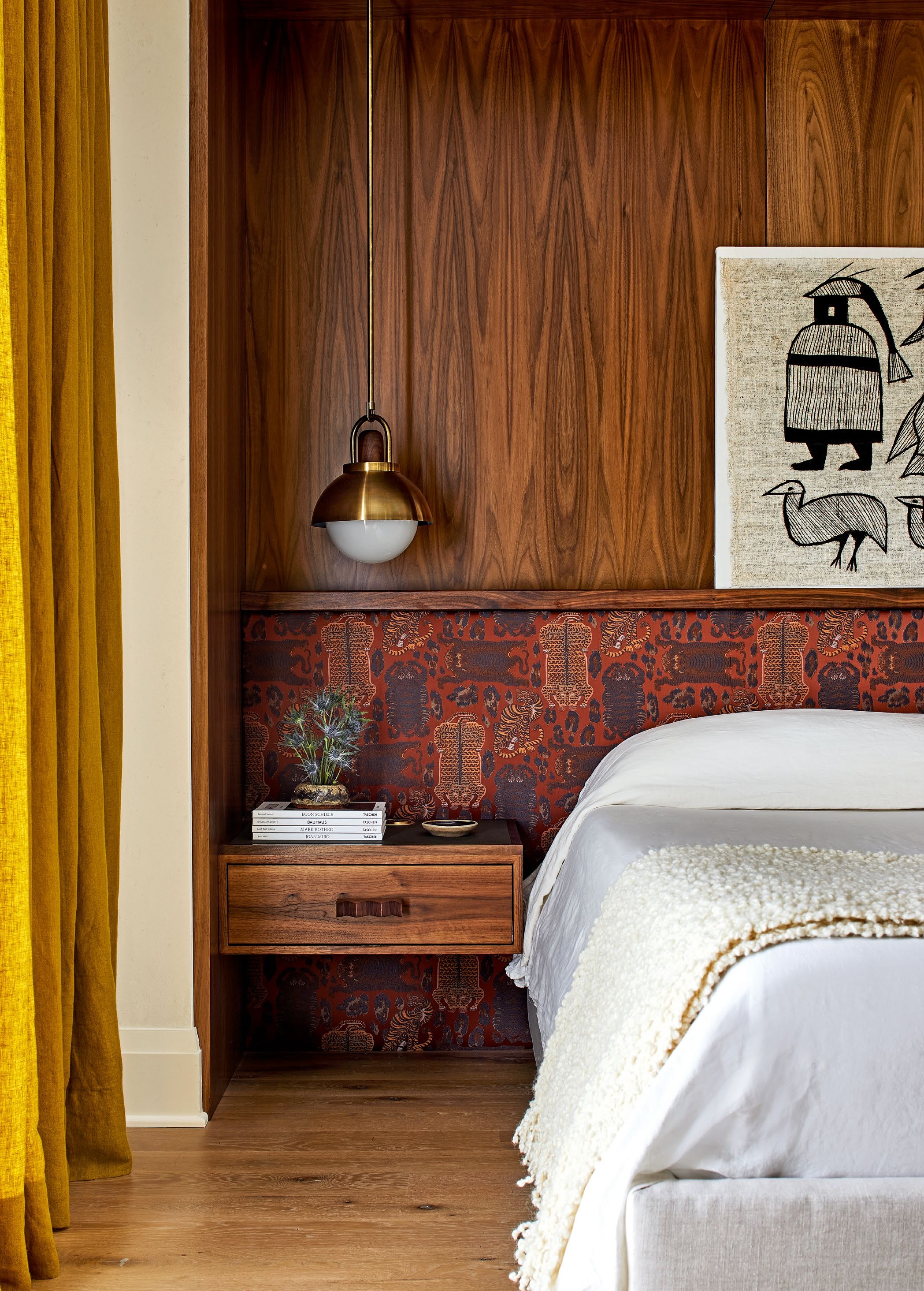 A cozy bedroom featuring walnut paneling, an Asian-inspired fabric headboard, mustard curtains, and a stylish pendant light, reflecting a warm and natural aesthetic.