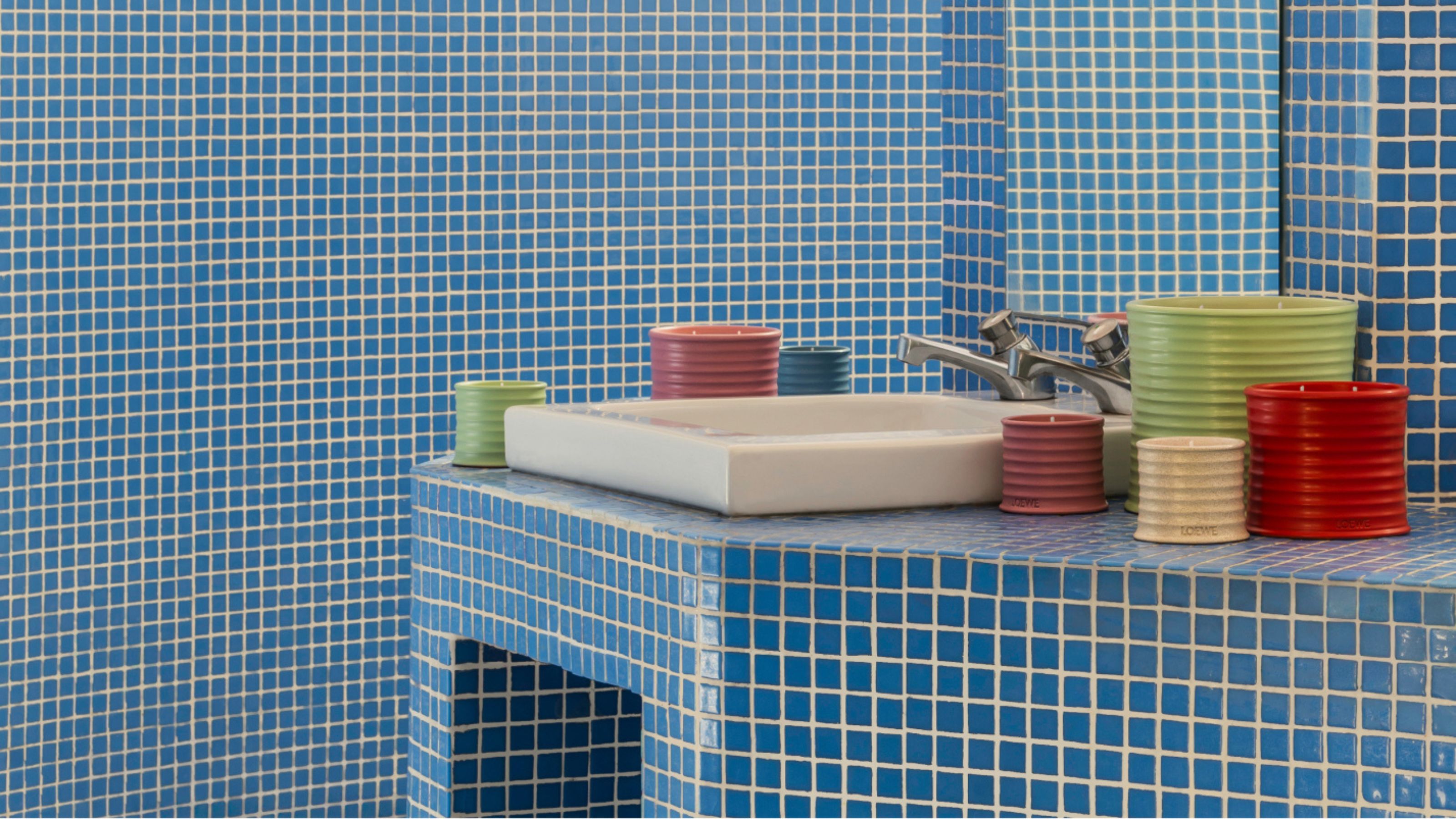blue tiled bathroom vanity with lots of loewe candles, a gray concrete sink, taps, and mirror