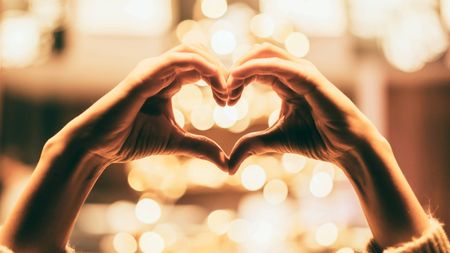 Hands held in a heart symbol against a blurred lights background