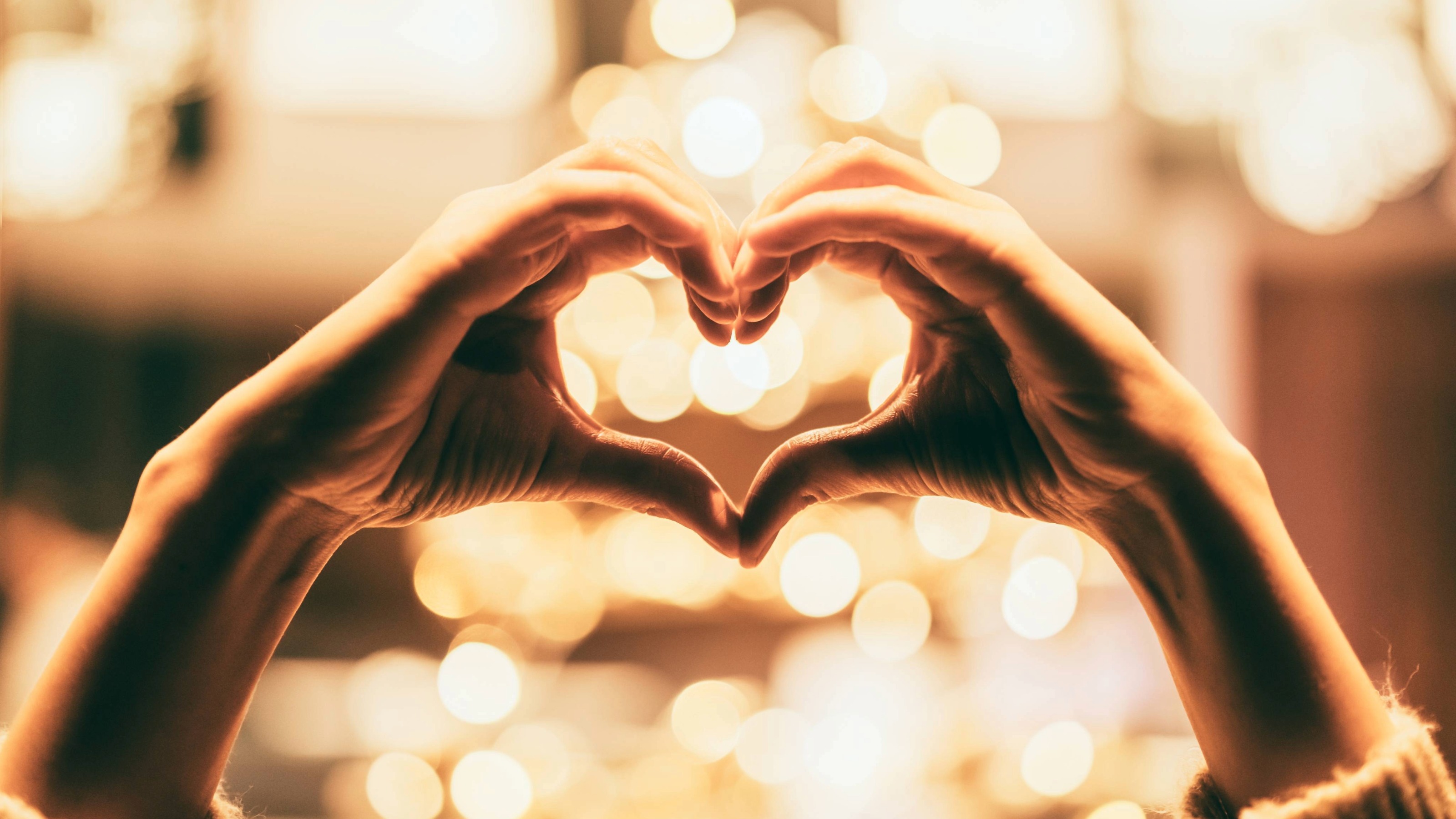Hands held in a heart symbol against a blurred lights background