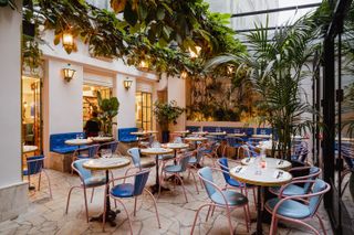 A covered courtyard with white walls blue and red bistro furniture and trailing greenery