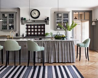 Black, white and gray kitchen with island, striped rug, black and white check backsplash and cabinet curtain and pale green gingham bar stools.