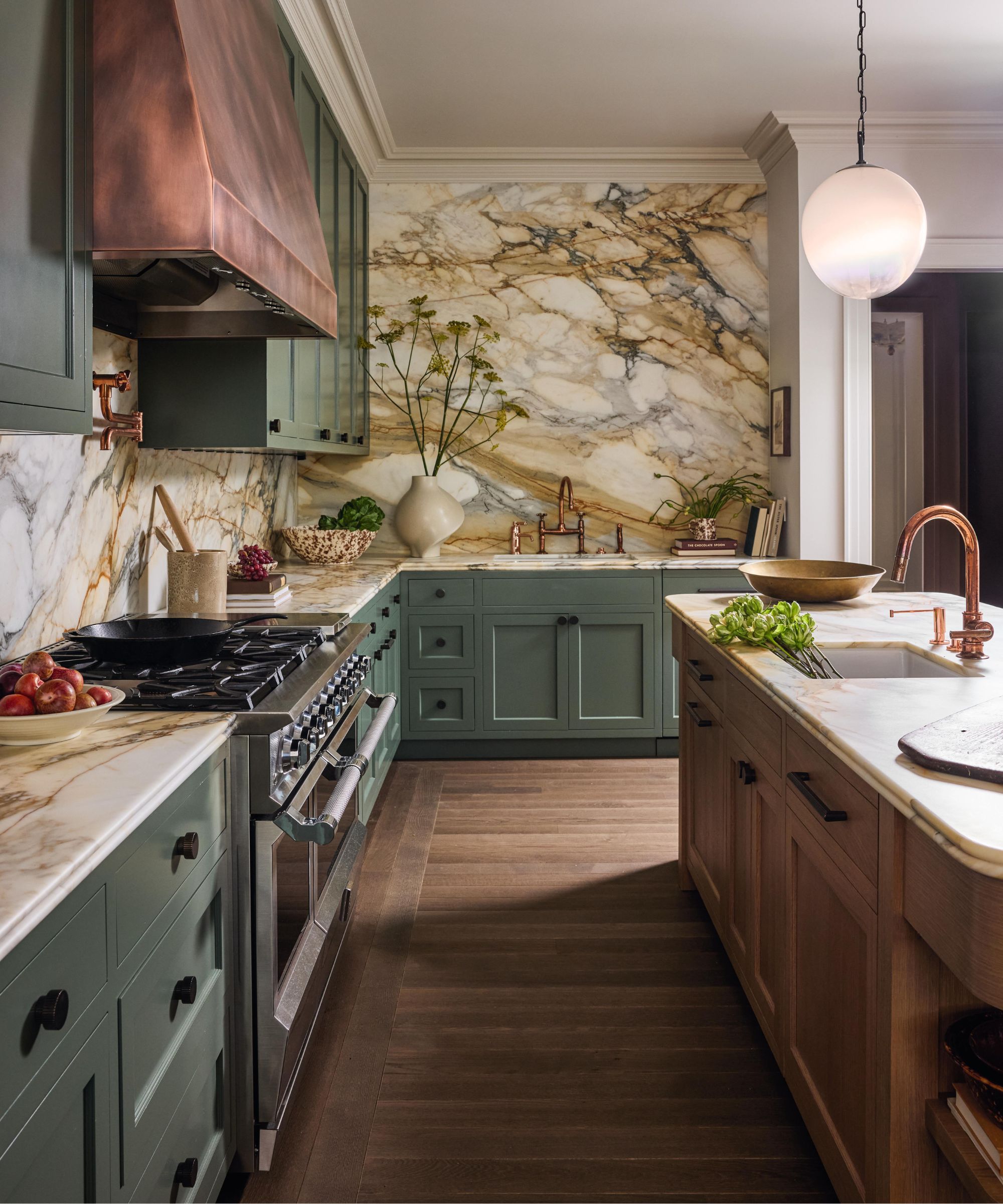 a large green and wood kitchen with statement marble walls and a copper cooker hood