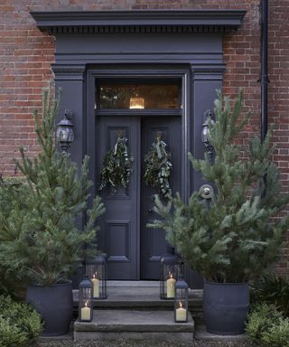 Christmas porch decor ideas with two bare Christmas trees either side of the door and lanterns on the steps