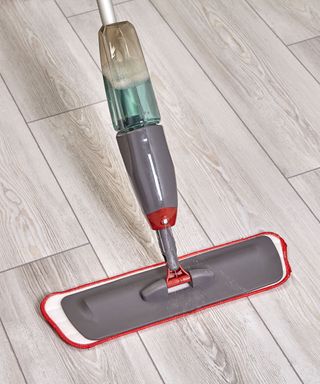 A gray and red spray mop on a gray wooden floor