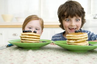 two children looking at pancakes stacked in front of them on table