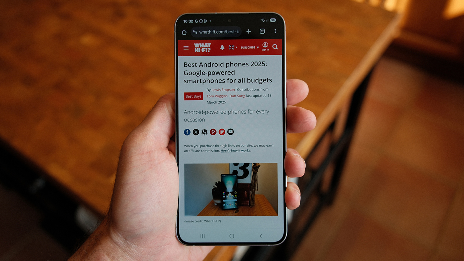 Samsung Galaxy S25 Plus smartphone held in hand showing What Hi-Fi? website on screen