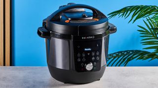 Instant Pot Plus photographed in front of a blue background.